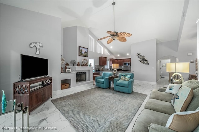 living room featuring arched walkways, marble finish floor, a fireplace, and a ceiling fan