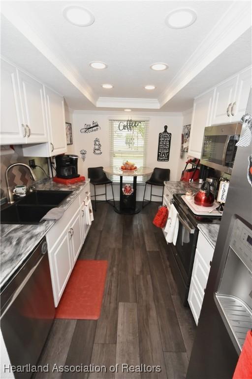 kitchen featuring a tray ceiling, stainless steel microwave, white cabinetry, a sink, and dishwasher