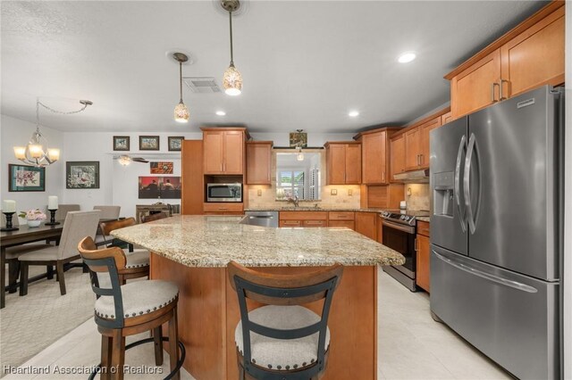 1904 Mulligan Rd, Sebring, FL 33872 - kitchen with appliances with stainless steel finishes, under cabinet range hood, light stone counters, a center island, and decorative backsplash