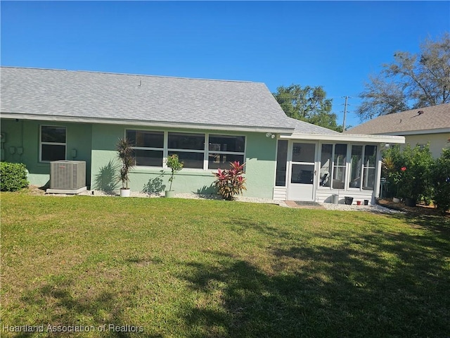 rear view of house featuring central air condition unit, stucco siding, a lawn, and a sunroom