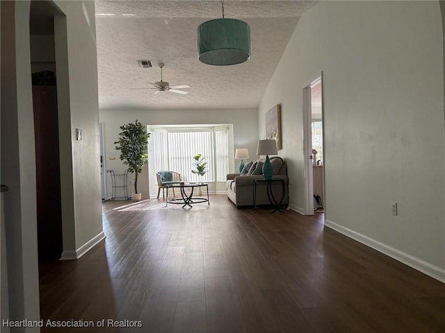 interior space featuring visible vents, a textured ceiling, dark wood-style floors, baseboards, and lofted ceiling