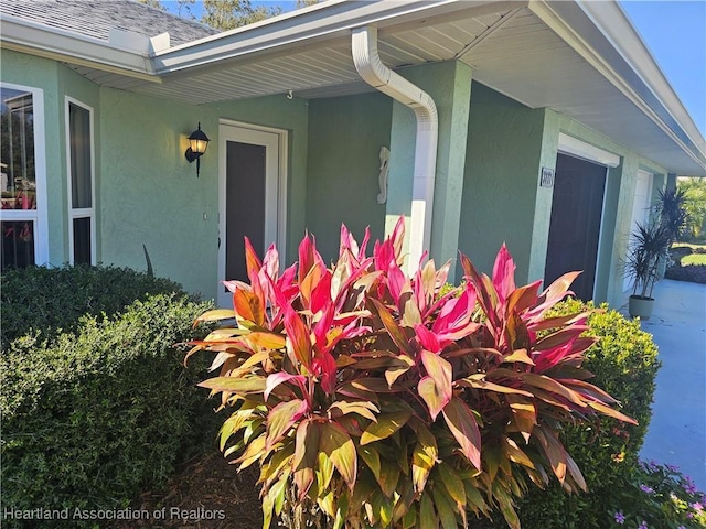 exterior details with roof with shingles, a downspout, gutters, and stucco siding