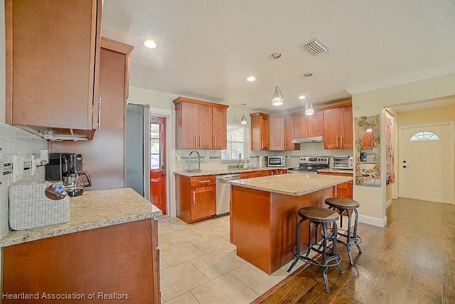 kitchen featuring visible vents, a kitchen island, under cabinet range hood, appliances with stainless steel finishes, and a kitchen breakfast bar