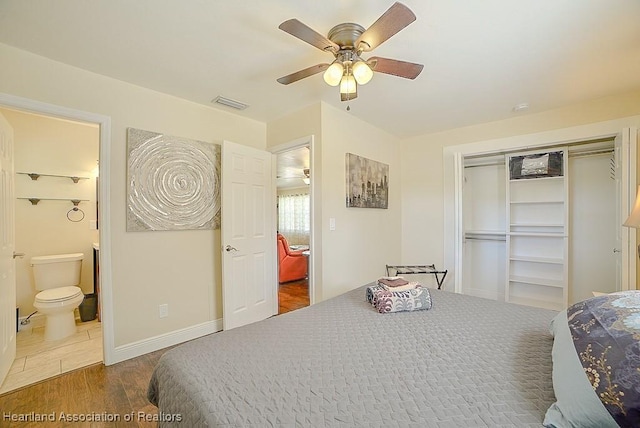 bedroom with wood finished floors, visible vents, baseboards, a closet, and ensuite bathroom