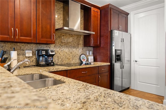 kitchen featuring light stone counters, stainless steel fridge with ice dispenser, wall chimney exhaust hood, and tasteful backsplash