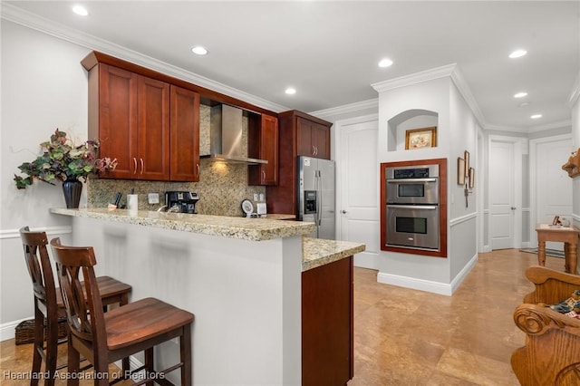 kitchen with tasteful backsplash, kitchen peninsula, appliances with stainless steel finishes, a breakfast bar area, and wall chimney exhaust hood