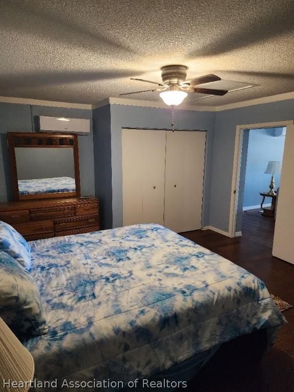 bedroom featuring ceiling fan, dark wood-type flooring, an AC wall unit, a textured ceiling, and a closet