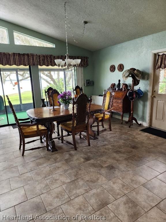 dining area with lofted ceiling, a textured ceiling, and a chandelier