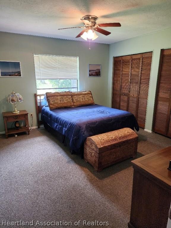 carpeted bedroom with a textured ceiling, ceiling fan, and multiple closets