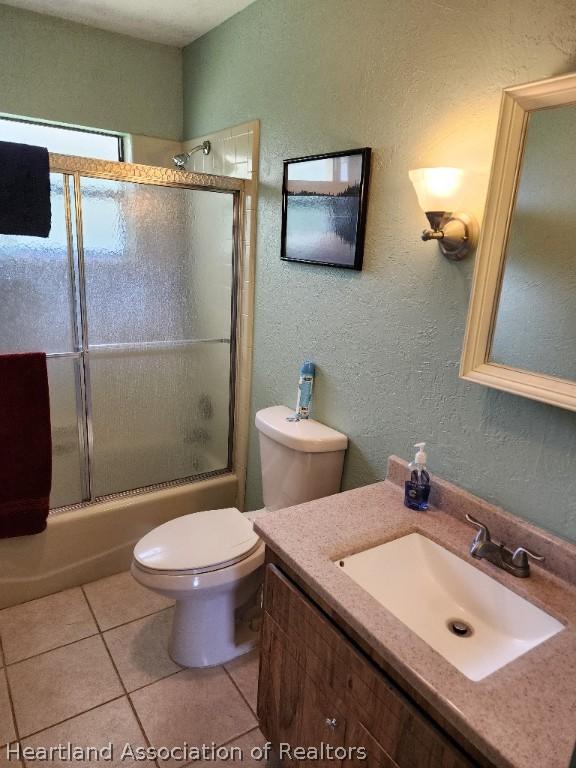 full bathroom with combined bath / shower with glass door, vanity, toilet, and tile patterned flooring