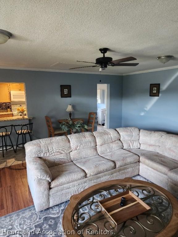 living room featuring hardwood / wood-style flooring, ceiling fan, ornamental molding, and a textured ceiling