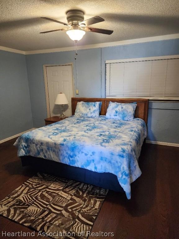 bedroom with a textured ceiling, dark wood-type flooring, ceiling fan, and crown molding