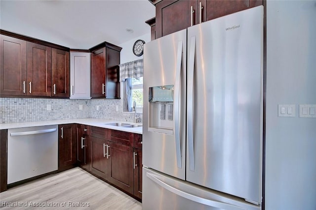 kitchen featuring appliances with stainless steel finishes, sink, decorative backsplash, dark brown cabinetry, and light hardwood / wood-style flooring