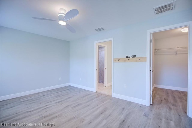 unfurnished bedroom with ceiling fan, a walk in closet, light hardwood / wood-style floors, and a closet