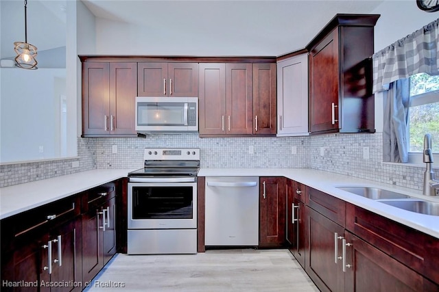 kitchen with appliances with stainless steel finishes, pendant lighting, sink, decorative backsplash, and light wood-type flooring