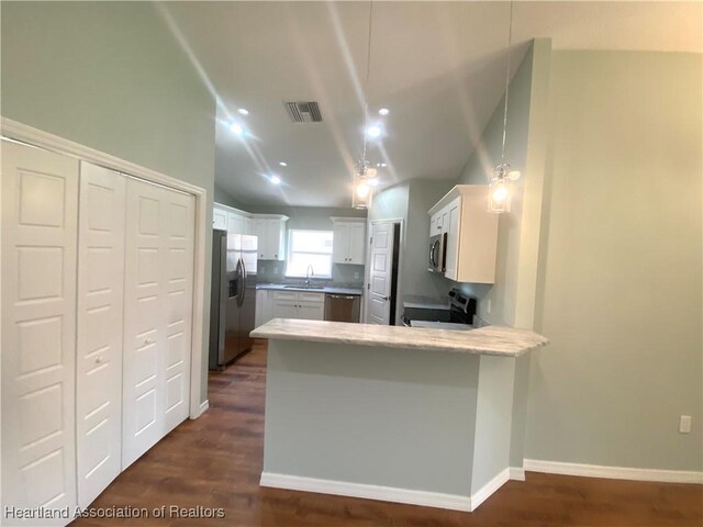 kitchen with dark wood-type flooring, vaulted ceiling, white cabinetry, kitchen peninsula, and stainless steel appliances