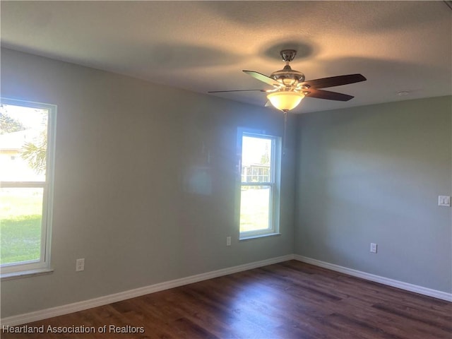 spare room featuring a ceiling fan, baseboards, and dark wood-type flooring