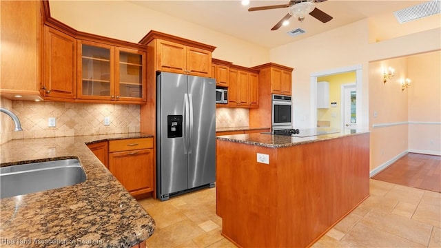 kitchen with visible vents, a kitchen island, glass insert cabinets, stainless steel appliances, and a sink