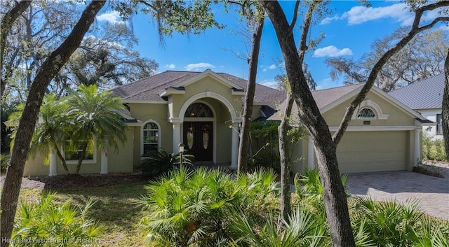 mediterranean / spanish house with french doors, decorative driveway, an attached garage, and stucco siding