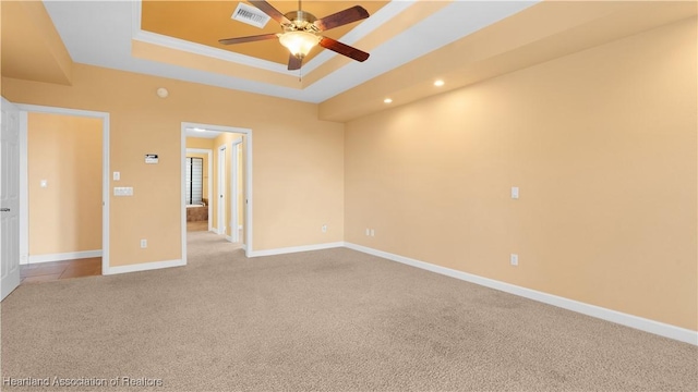 empty room featuring a tray ceiling, light colored carpet, visible vents, a ceiling fan, and baseboards