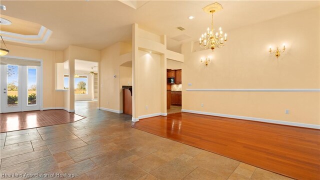 spare room featuring arched walkways, stone tile floors, ceiling fan with notable chandelier, baseboards, and a tray ceiling