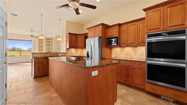 kitchen featuring stainless steel appliances, a kitchen island, brown cabinets, dark stone countertops, and decorative light fixtures