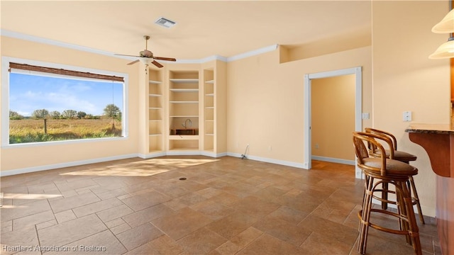 spare room with built in shelves, visible vents, ornamental molding, ceiling fan, and baseboards