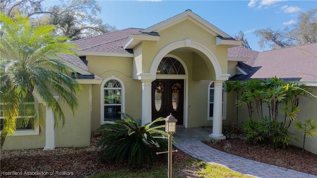 view of exterior entry with roof with shingles and stucco siding