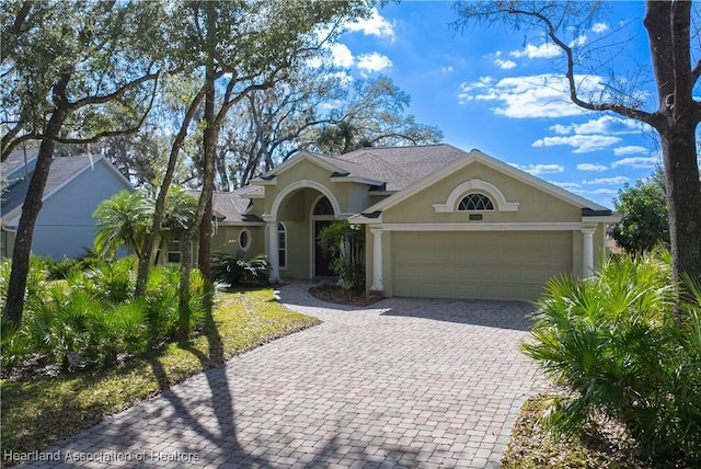 view of front of home with decorative driveway, an attached garage, and stucco siding