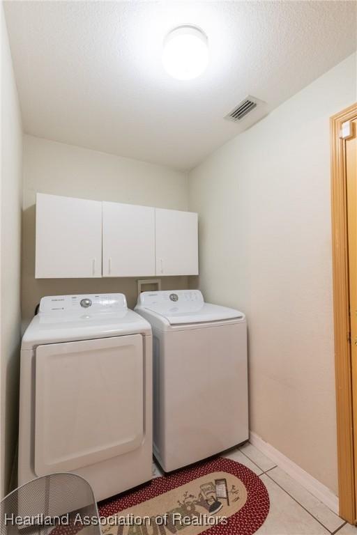 clothes washing area with cabinets, washing machine and clothes dryer, and light tile patterned floors