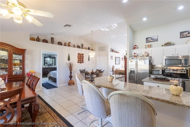 kitchen featuring light tile patterned flooring, appliances with stainless steel finishes, white cabinetry, lofted ceiling, and light stone counters