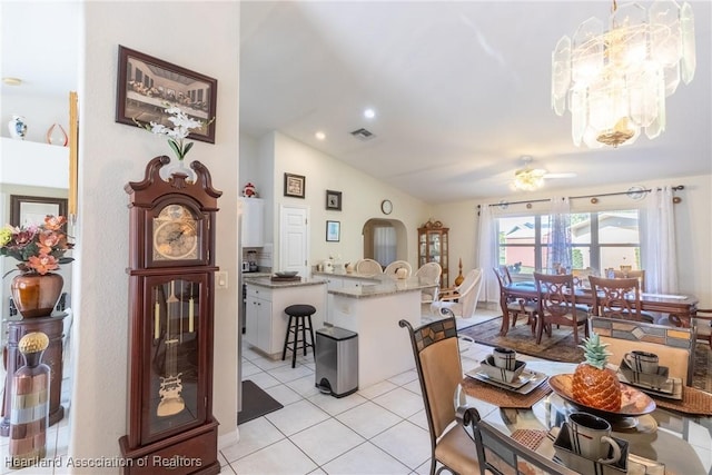 dining space with ceiling fan with notable chandelier, vaulted ceiling, and light tile patterned flooring