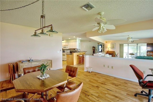 dining space featuring a textured ceiling, visible vents, a ceiling fan, and light wood-style floors