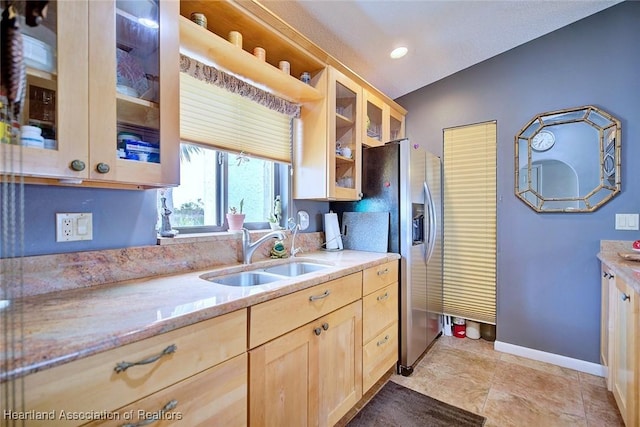 kitchen with lofted ceiling, stainless steel refrigerator with ice dispenser, sink, light stone countertops, and light brown cabinets