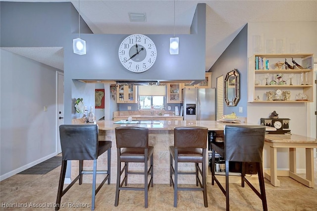 kitchen featuring kitchen peninsula, a kitchen bar, stainless steel fridge, and decorative light fixtures