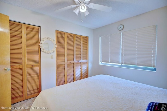 bedroom featuring ceiling fan, a textured ceiling, and multiple closets