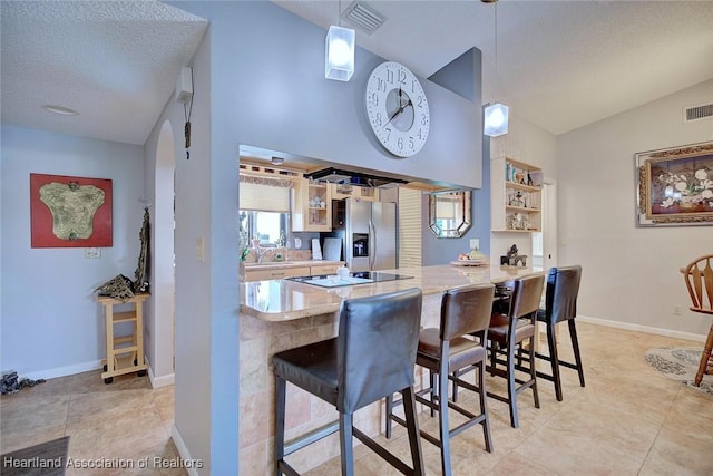 kitchen with a textured ceiling, stainless steel fridge with ice dispenser, kitchen peninsula, black electric cooktop, and a breakfast bar area