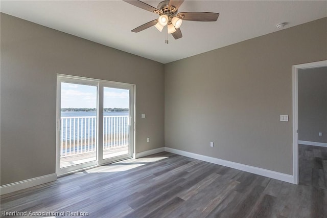 unfurnished room featuring dark hardwood / wood-style flooring, ceiling fan, and a water view