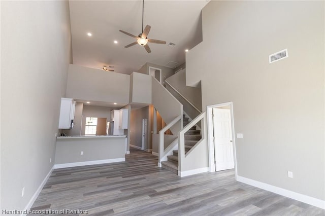 unfurnished living room with a towering ceiling, hardwood / wood-style flooring, and ceiling fan