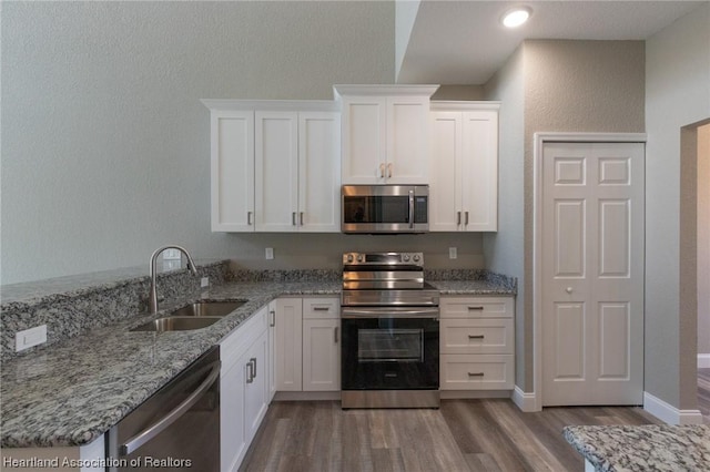 kitchen featuring light stone countertops, white cabinetry, sink, stainless steel appliances, and hardwood / wood-style floors