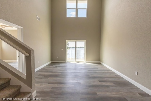 unfurnished living room with a high ceiling, ceiling fan, and wood-type flooring