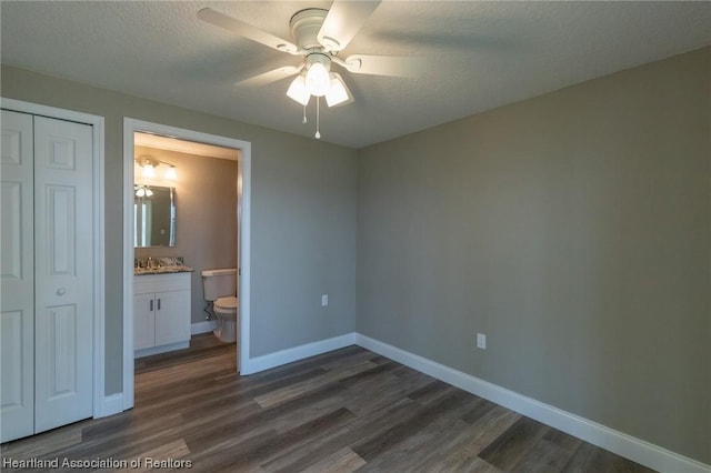 unfurnished bedroom featuring ensuite bath, ceiling fan, dark wood-type flooring, a textured ceiling, and a closet