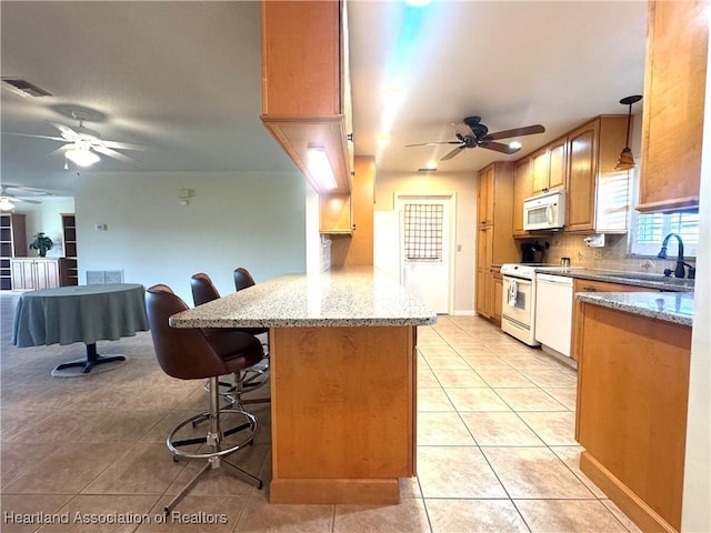 kitchen with white appliances, light tile patterned floors, sink, decorative light fixtures, and a breakfast bar