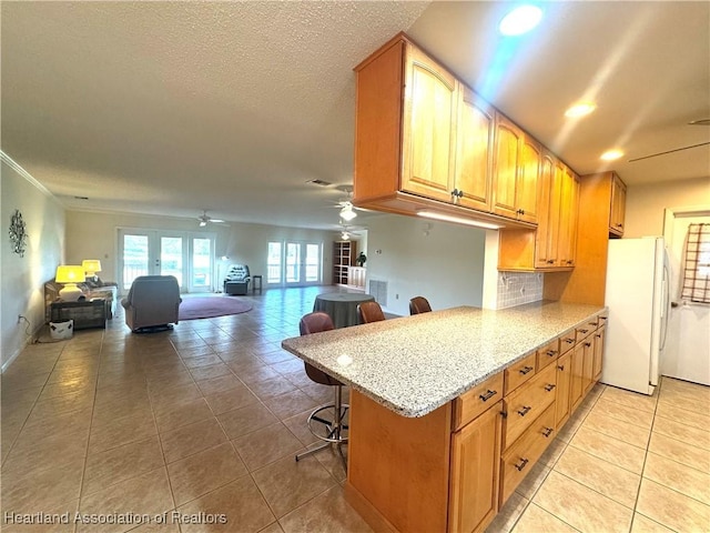 kitchen with kitchen peninsula, white refrigerator, tasteful backsplash, light stone counters, and a breakfast bar