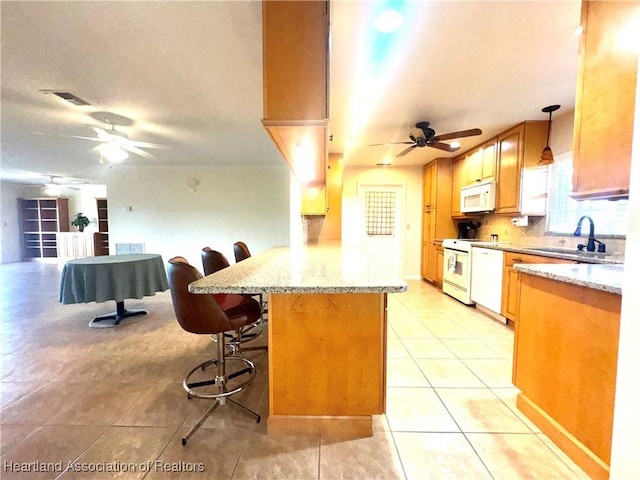 kitchen featuring white appliances, sink, decorative light fixtures, ceiling fan, and a breakfast bar area