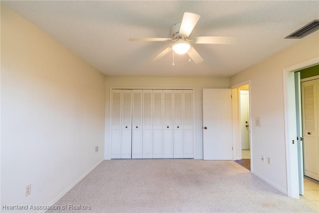 unfurnished bedroom featuring a textured ceiling, a closet, ceiling fan, and light colored carpet