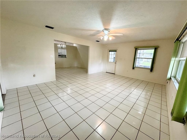 empty room with light tile patterned floors, a textured ceiling, and ceiling fan with notable chandelier