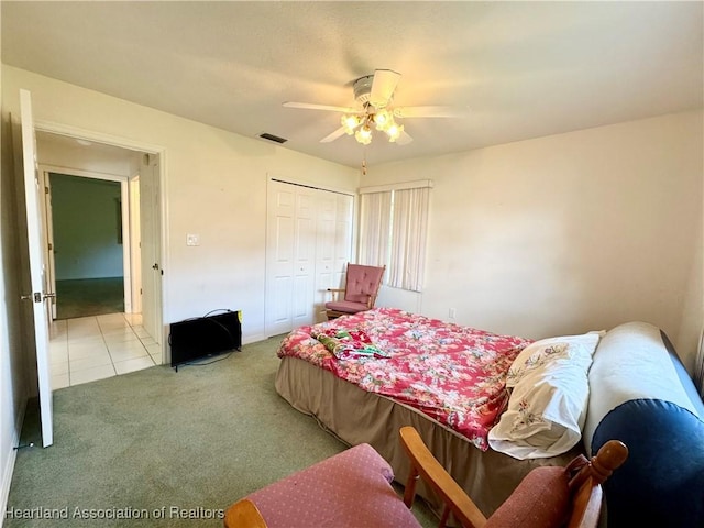 bedroom featuring ceiling fan, light tile patterned floors, light colored carpet, visible vents, and a closet