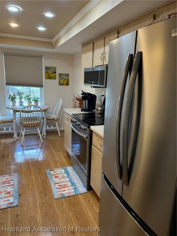 kitchen with appliances with stainless steel finishes, ornamental molding, a tray ceiling, light countertops, and light wood-type flooring