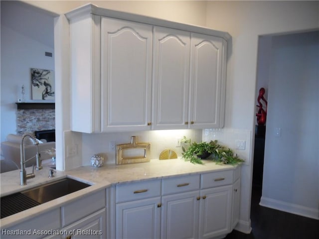 kitchen with white cabinetry, tasteful backsplash, light stone countertops, and a sink
